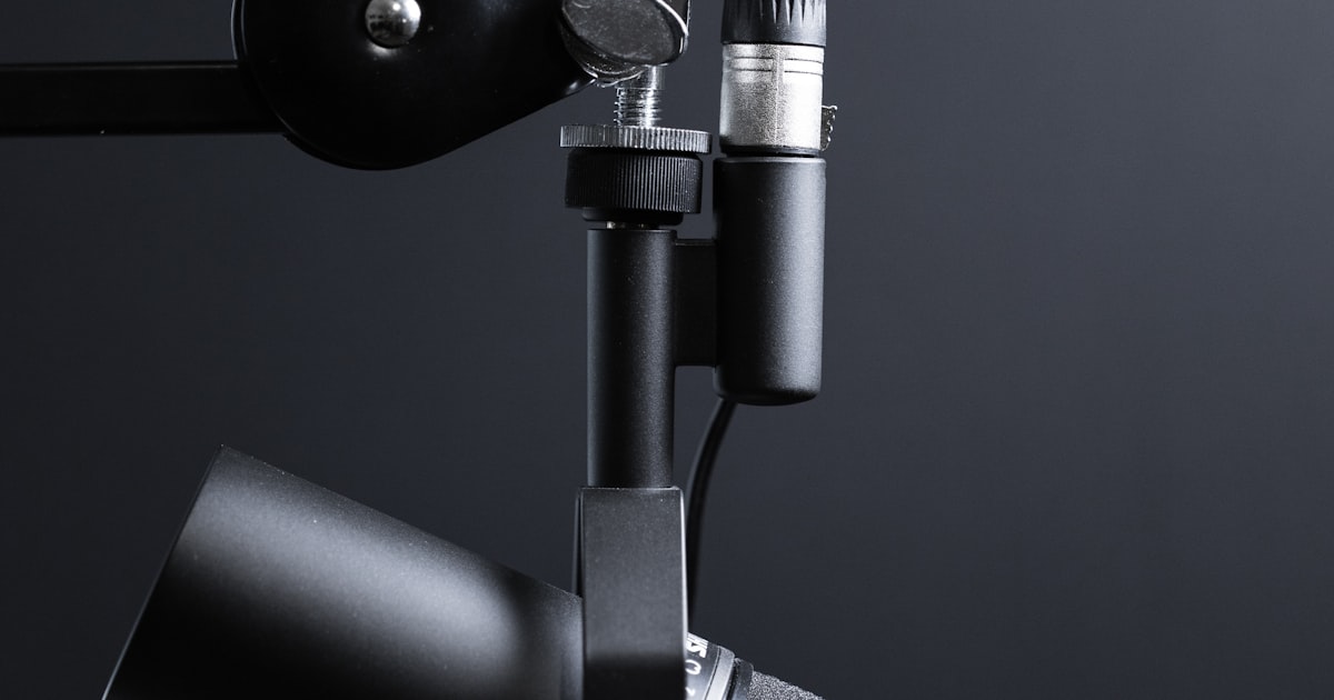 A clean podcast recording setup with a professional microphone, headphones, and laptop on a desk with acoustic treatment